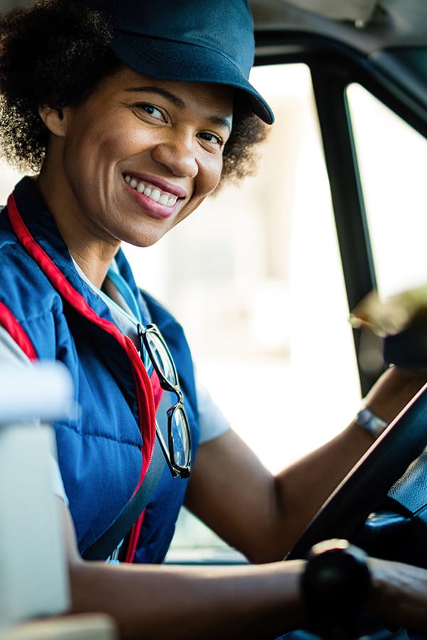 Happy black female courier driving delivery van and looking at camera.